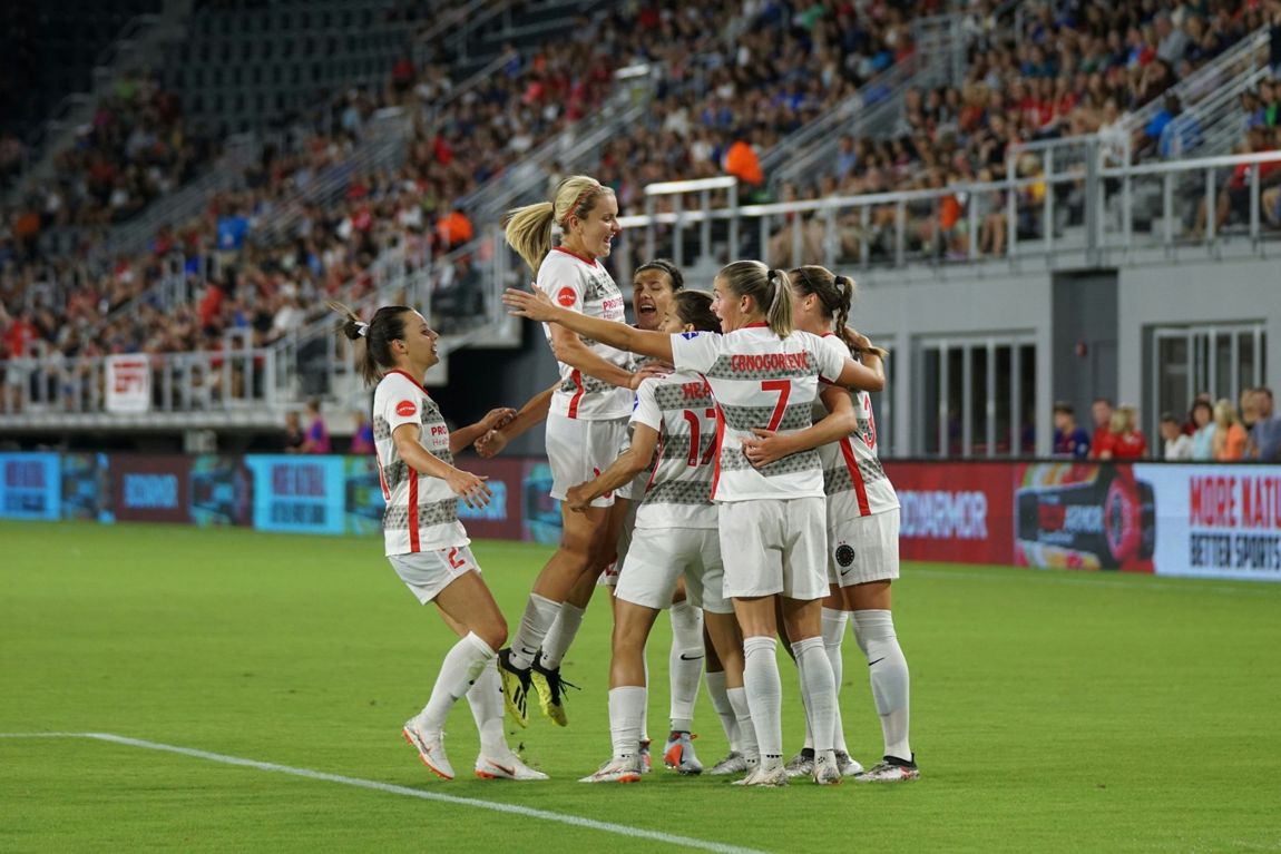 Women's football team celebrating a goal in front of a full stand